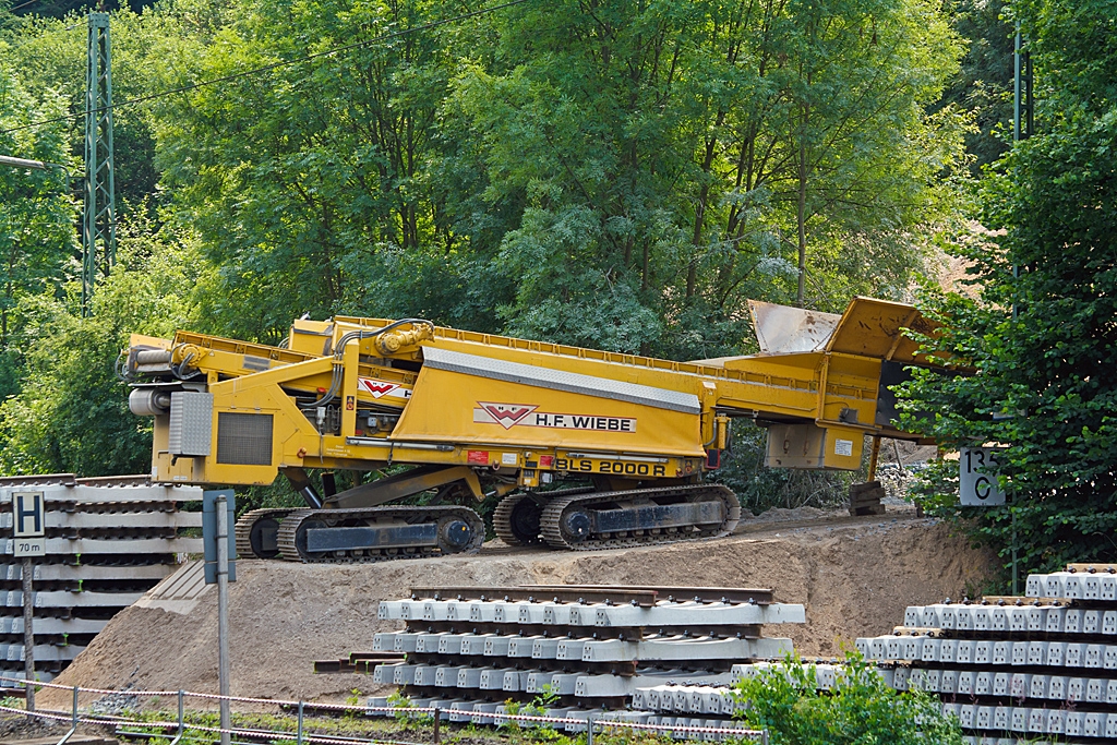 Plasser & Theurer Beladestation BLS 2000 R (mit Raupenfahrwerk) der H.F. Wiebe am 13.07.2013 beim Bahnhof Sinn (Lahn-Dill-Kreis).

Die Beladestation ist zum Verladen von Schotter, Kies und PSS-Material in MSF-Wagen (Materialfrder- und Silowagen) oder Schttgutwagen, dies ist auch unter vorhandener, abgeschalteter Oberleitung mglich. Dabei wird Material (z.B. mittels Radlader) in den Schottertrichter aufgegeben. Vom ersten Frderband auf das zweite hydraulisch ausfahrbares Frderband transportiert, von dem dann das Material in die entspr. Wagen abfllt. Der ganze Rahmen ist auf zwei Raupenfahrwerken und ist hydraulisch heb- und senkbar.

Die Frderbnder, wie auch die Raupenfahrwerke werden hydraulisch angetrieben, die Energie dazu liefert ein Dieselmotor mit 148 kW Leistung. Die Beladestation wiegt ca. 30.000 kg und ist 12.600 mm lang.
