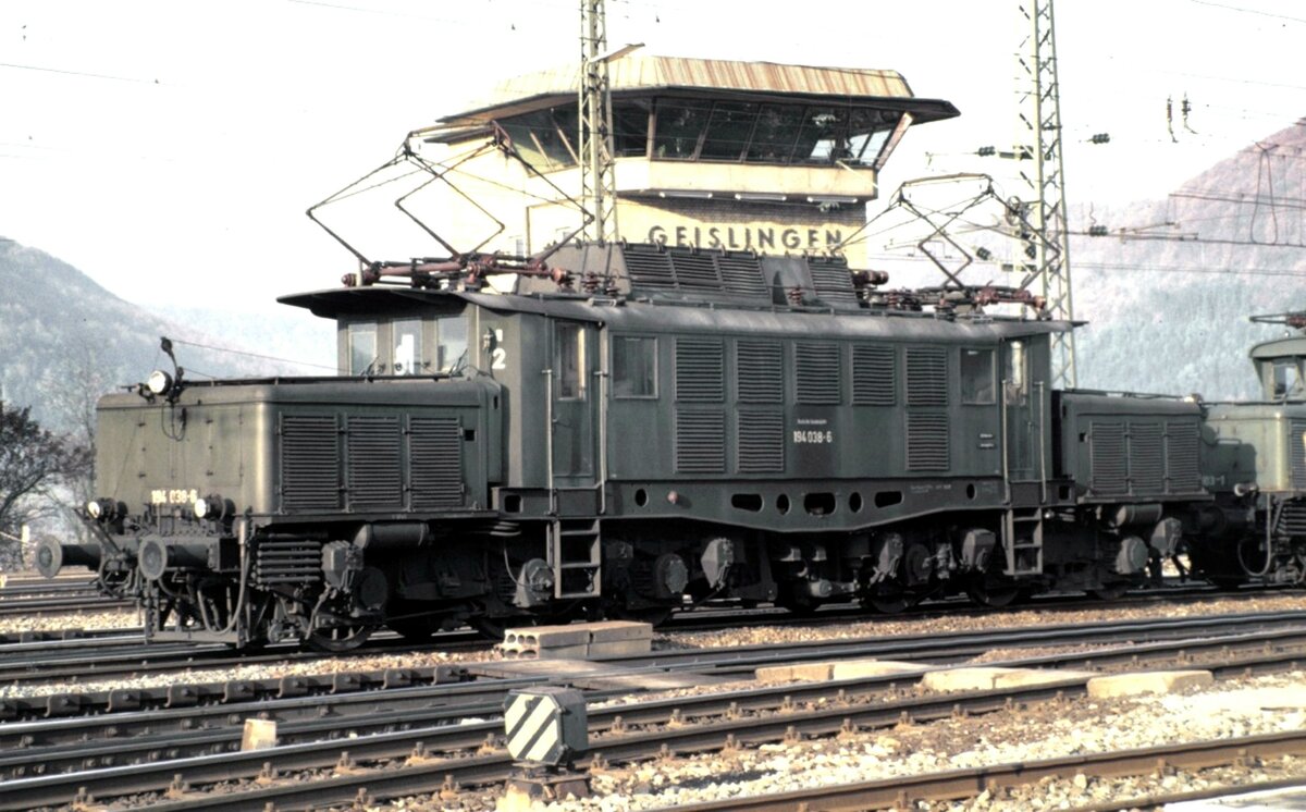 194 038-6 Schublok auf der Geislinger Steige, noch mit Kupplungsüberwurfbügel und Seilzug in den Führerstand ausgerüstet, am 11.10.1980.
Der Kupplungsüberwurfbügel war Ende 1980 bereits nicht mehr im Einsatz, da sich herausstellte, das der Bügel sich sehr leicht verhakt hat und nicht über Seilzug gelöst werden konnte. Um die Schublok vom Zug zu Lösen war ein Halt im nächsten Bahnhof mit Ausweichstelle. Das waren Westerstetten oder Ulm. So kam es vor,dass die Schublok bis Ulm mitgeschleppt wurde.
Die Einrichtung wurde bald wieder abgebaut. Somit haben diese Fotos einen gewissen Seltenheitswert.