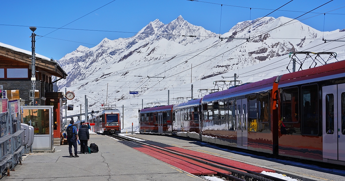 Am 10.05.2024 kreuzen sich in der Station Riffelberg zwei Zge der Gornergratbahn: Im Hintergrund kommen der Bhe 4/6 3084 und ein weiterer Bhe 4/6 an, auf dem Nebengleis warten die Bhe 4/6 3094 und 3095 auf die Weiterfahrt nach Zermatt. In der Bildmitte die Mischabelgruppe mit dem Dom (mit 4545 m der hchste Gipfel der Schweiz, der komplett auf schweizer Gebiet liegt) und Tschhorn (4491 m), rechts der Alphubel (4206 m). 