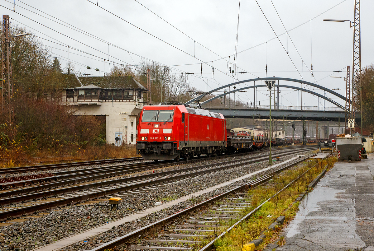 
Bei Regen....
Die DB Cargo 185 315-9 (91 80 6185 315-9 D-DB) verlässt am 08.12.2018 mit einem langen leeren Coilzug den Gbf Kreuztal in Richtung Hagen. 
Für einen beladenen Zug in der Länge und auf dieser Strecke (Ruhr-Sieg-Strecke) hätte die Zugkraft der TRAXX F140 AC2 wohl allein kaum ausgereicht. 

Im Hintergrund das ehemalige Fahrdienstleiter Reiterstellwerk Kreuztal (Kf), es wurde 1923 in Betrieb genommen und steht unter Denkmalschutz.