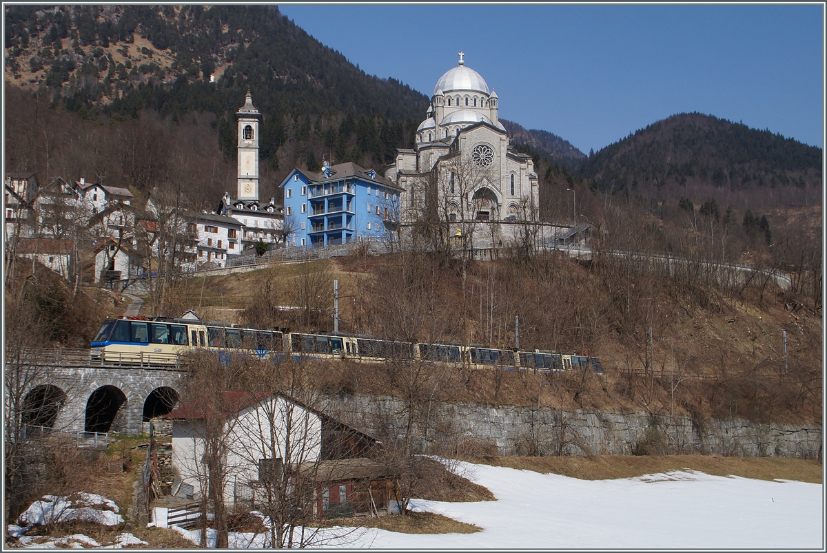 Der SSIF Treno Panoramico Vision Vigezzo vor der Kulise der Wahlfahrtskirche  Madonna del Sangue  in Re. Zwischen von hier einige hundert Meter westliche gelegenen Bahnhof Re und dem  in der Schweiz liegenden Camedo verkehren bis auf wenige Ausnahmen nur die internationalen Züge, das der Regionalverkehr von Domodossola und Locarno in den vorgenannten Stationen endet. 
19. März 2015