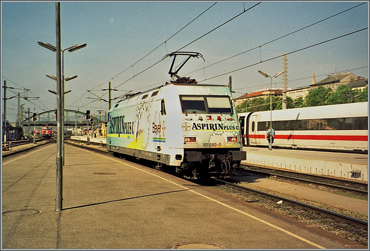 Die DB 101 080 wirbt in Wien Westbahnhof farbenfroh für  Aspirin C-Plus . 

Analogbild vom l. Mai 2001