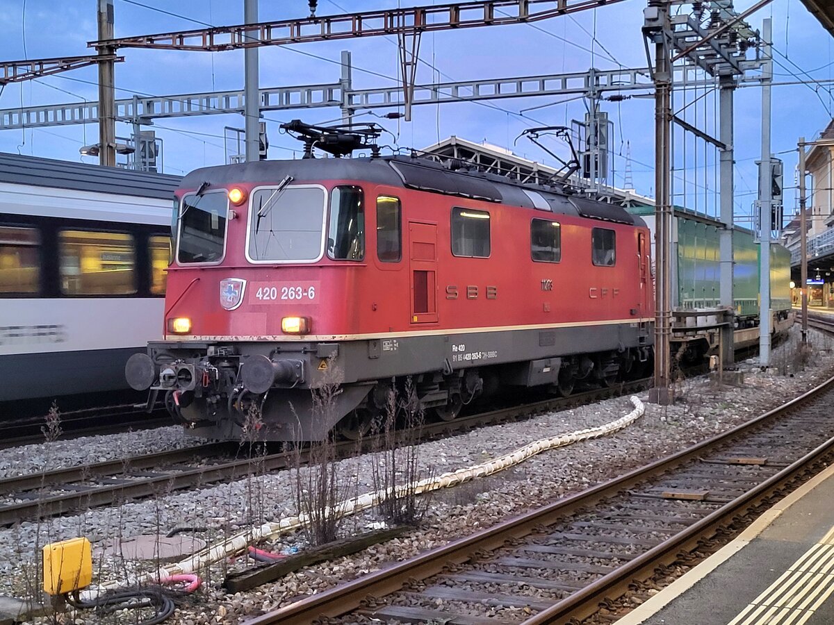 Die SBB Re 4/4 II 11263 (Re 420 263-6), welche mit einer automatischer Kupplung vom Typ Scharfenberg ausgestattet ist, wartet in Lausanne mit einem Güterzug, der ebenfalls über automatische Kupplungen verfügt, auf die Weiterfahrt nach St-Triphon. 

8. März 2025