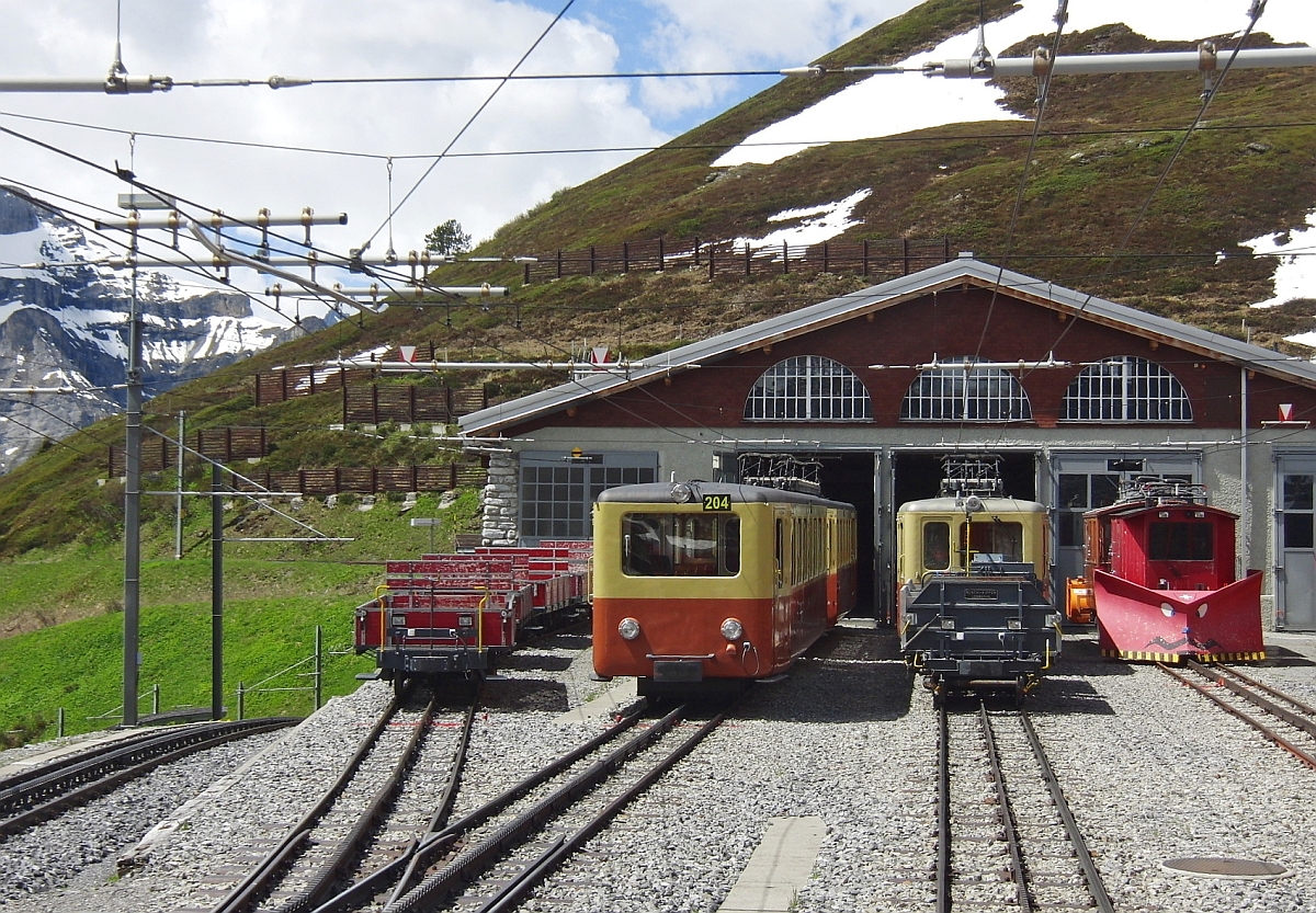 Fahrzeugparade vor dem Lokschuppen der Jungfraubahn auf der Kleinen Scheidegg am 15.06.2013. Aufnahme entstand aus dem zum Jungfraujoch abfahrbereiten Triebwagen.