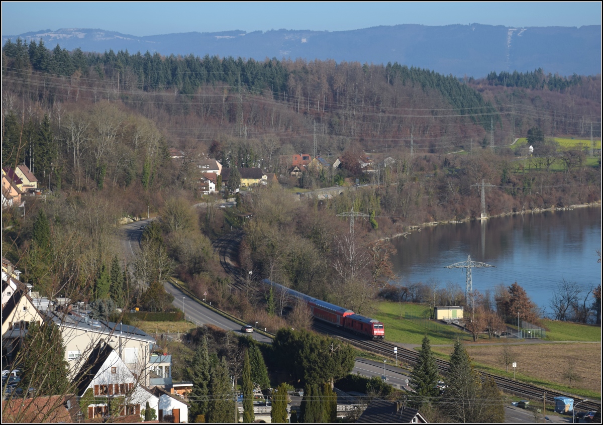 Godot-Express rechts des Hochrheins.

Eine BR 245 mit 3 Dostos. Karsau, Dezember 2021.

An jeder Station wird neuerdings erneut auf Godot gewartet. Er könnte ja noch kommen, auch wenn ihn bis heute niemand gesehen hat. Reisen im 612 war gestern, heute heißt es durch die Landschaft bummeln. Beachtenswert noch: Entgegen der Versprechung leichter und schneller Einstieg fährt hier ein Hocheinstiegsdosto mit. Sehr geschickt bei den besseren Bordsteinen in den Bahnhöfen der Hochrheinbahn. So macht es keinen Unterschied zu den Einstiegszeiten der 612er.