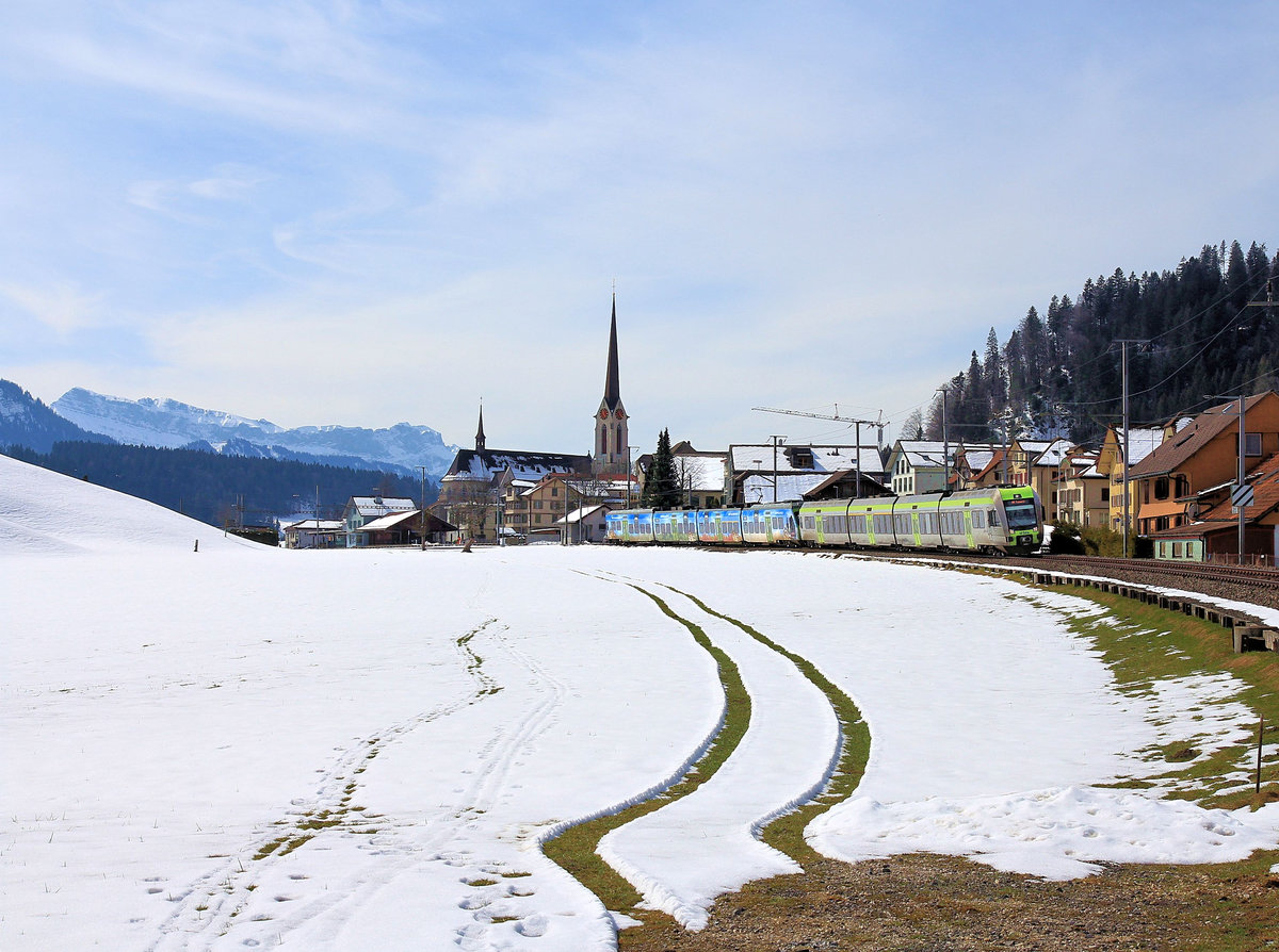Im Entlebuch: Escholzmatt mit der Silhouette der - für das luzerner Land typischen - riesigen Kirche. Der Regionalexpress Bern - Luzern wird vom Lötschberger Nr. 106 geführt, mit BLS NINA 015 an zweiter Stelle. 25.März 2021 