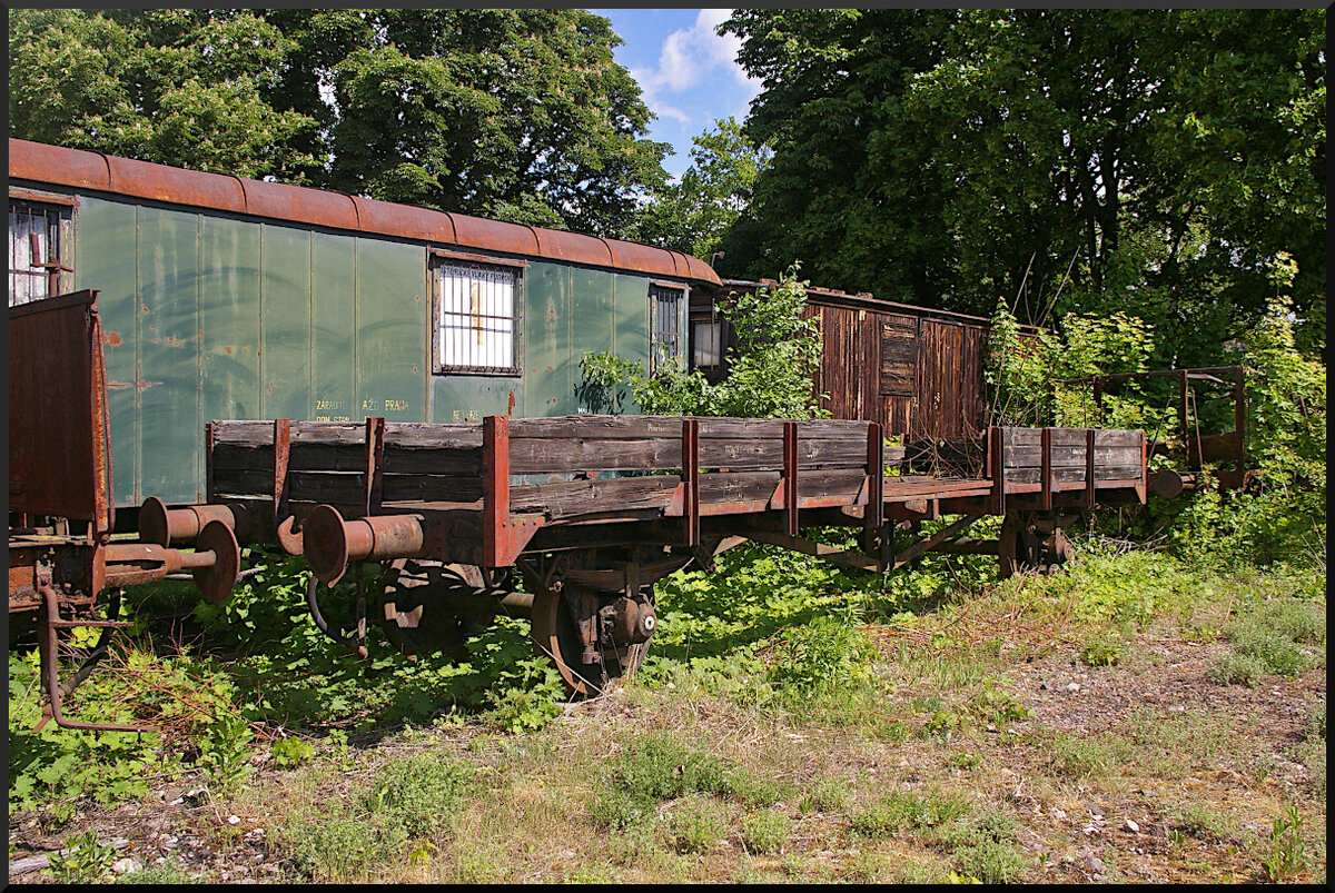 Im vorderen Bereich des Eisenbahnmuseum Jaroměř findet sich dieser hölzerne Niederbordwagen, dem die Witterung schon sehr zugesetzt hat. Dahinter etwas schief und abgesackt umgebaute Personenwagen für den Bahndiensteinsatz.

Eisenbahnmuseum Jaroměř, 21.05.2022
