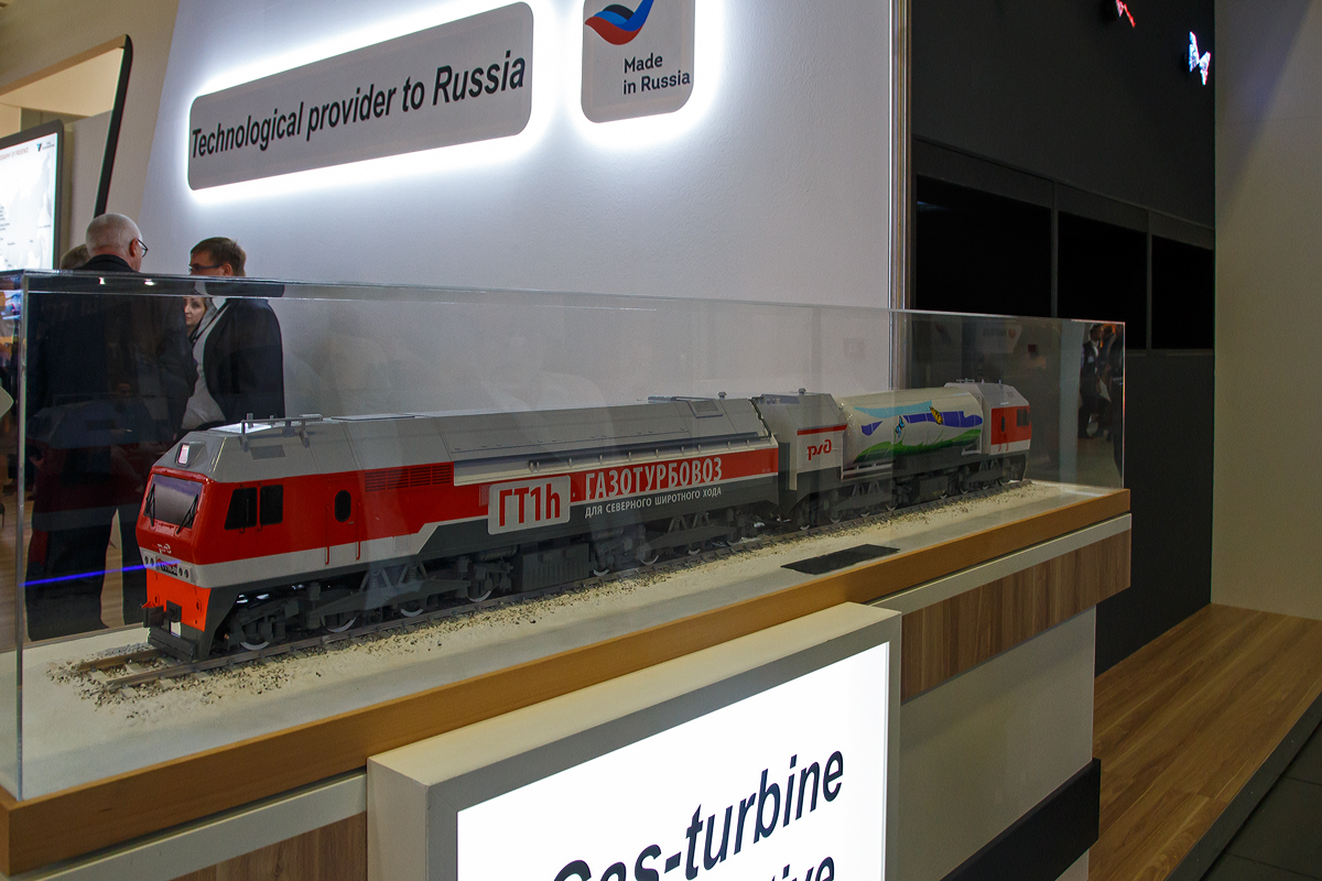 Leider nur als Modell ausgestellt auf der InnoTrans 2018 (hier 18.09.2018) die mächtige 16-achsige russische RŽD Gasturbinen-Lokomotive  ГT1h-002 (GT1h-002).

Die Lokomotiven der RŽD-Baureihe ГT1h (deutsche Transkription GT1h) der Russischen Eisenbahnen (RŽD) sind schwere Gasturbinenlokomotiven mit elektrischer Kraftübertragung, vorrangig für den Güterzugdienst. Sie sind bestimmt für den schweren Güterzugdienst auf nichtelektrifizierten Abschnitten, vorrangig in Sibirien. Bisher wurden zwei Fahrzeuge gebaut, mit denen umfangreiche Versuche durchgeführt wurden. Die Kraftübertragung geschieht von einer Gasturbine aus, die mit verflüssigtem Erdgas betrieben wird, an ihr ist ein Wechselstrom-Generator angeschlossen, der produzierte Strom wird gleichgerichtet für die Speisung der Traktionsfahrmotoren verwendet. Es ist eine Serie von 40 Fahrzeugen bestellt.

Die Leistung der ГT1 beträgt 8.300 kW, damit gilt die Lokomotive als die leistungsstärkste Gasturbinenlokomotive der Welt. Die überarbeitete ГТ1h.002 besitzt eine Anfahrzugkraft von 980 kN, die Zugkraft im Dauerleistungs-Regime (bei 33 km/h) beträgt 775 kN.

Die Ausarbeitung begann im 2005 nach der Unterzeichnung des Vertrages zwischen der RŽD und der All-Russian Rolling Stock Design and Technology Research Institute. Spezialisten der Kompanie Kusnezow schufen die starke Gasturbine НК-361 (NK-361) und den Antriebsblock der Gasturbinenlok. 2007 entstand die erste Versuchslokomotive, die auf der Basis der ВЛ15.008 hergeleitet wurde. Die Gasturbine entstand in Samara, die Montage der Lokomotive wurde in dem Ausbesserungswerk Woronesch durchgeführt. Die neue Lokomotive bekam die Bezeichnung ГT1-001 zuerkannt. Die Lokomotive hat eine Dienstgewicht von 300 t und einen Kraftstoffvorrat von 17 Tonnen. 
Am 4. Juli 2008 beförderte die ГT1-001 zum ersten Mal eine Güterzugeinheit. Die Masse des Zuges betrug 3.000 t, und die Überprüfung wurde auf dem Abschnitt Kinel–Schigulewskoe More der Eisenbahn im Oblast Kuibyschew durchgeführt. Damals war geplant, dass die ersten Gasturbinenloks in Sibirien zum Einsatz kommen werden, wo die meisten Vorkommen von Erdgas lagern. Am 22. Dezember 2008 fuhr sie zum ersten Mal einen Güterzug mit einer Masse von 10.000 t, bestehend aus 116 Wagen. Ein Güterzug mit einer Masse von 15.000 t, bestehend aus 159 Wagen wurde zum ersten Mal am 23. Januar 2009 gefahren. 
Am 12. Oktober 2009 erhielt die RŽD im Guinness-Buch der Rekorde ein Diplom für den Bau der leistungsstärksten Gasturbinenlok der Welt, die mit verflüssigtem Erdgas angetrieben wird. 
Am 7. September 2011 fuhr auf dem Gleisring des VNIIZhT in Schtscherbinka ein Güterzug mit einer Masse von 16.000 t, bestehend aus 170 Wagen, was einige Institutionen in Russland fehlerhaft als Weltrekord auslegten. 
Im Jahr 2012 erfolgte, mit dem Ersatz der Diesel-Krafteinheit für die Erstellung der Hilfsenergie durch eine Akku-Batterie, eine Modernisierung. Seit der Zeit besitzt die Lokomotive den Index h (hybrid). 
Ab August 2013 lieferte die Diesellokfabrik Ljudinowo eine Serienausführung der Gasturbinenlokomotive aus, die die Bezeichnung ГT1h-002 erhielt. Die Serienausführung hat eine Dienstgewicht von 368 t und einen Kraftstoffvorrat von 20 Tonnen.

TECHNISCHE DATEN:
Spurweite: 	1.520 mm (Breitspur)
Achsformel: (Bo’Bo’) (Bo’Bo’) + (Bo’Bo’) (Bo’Bo’
Länge über Kupplung: 2 × 21.500 mm
Drehzapfenabstand:  10.900 mm
Achsstand im Drehgestell:  6.300 mm (3 × 2.100 mm)
Treibraddurchmesser: 	1.050 mm (neu)
Höhe:  5.250 mm
Breite: 3.150 mm
Dienstgewicht: 2×184 t = 368 t
Radsatzfahrmasse:  23,5 t 
Leistung: 8.300 kW
Dauerleistung: 6.458 kW
Anfahrzugkraft: 980 kN
Dauerzugkraft: 775 kN bei 30 km/h
Höchstgeschwindigkeit: 100 km/h
Motorentyp:  Gasturbine vom Typ  NK-361
Nenndrehzahl: 6.000 U/min
Leistungsübertragung: elektrisch
Tankinhalt:  20 t
Anzahl der Fahrmotoren: 16 Gleichstrommotore
