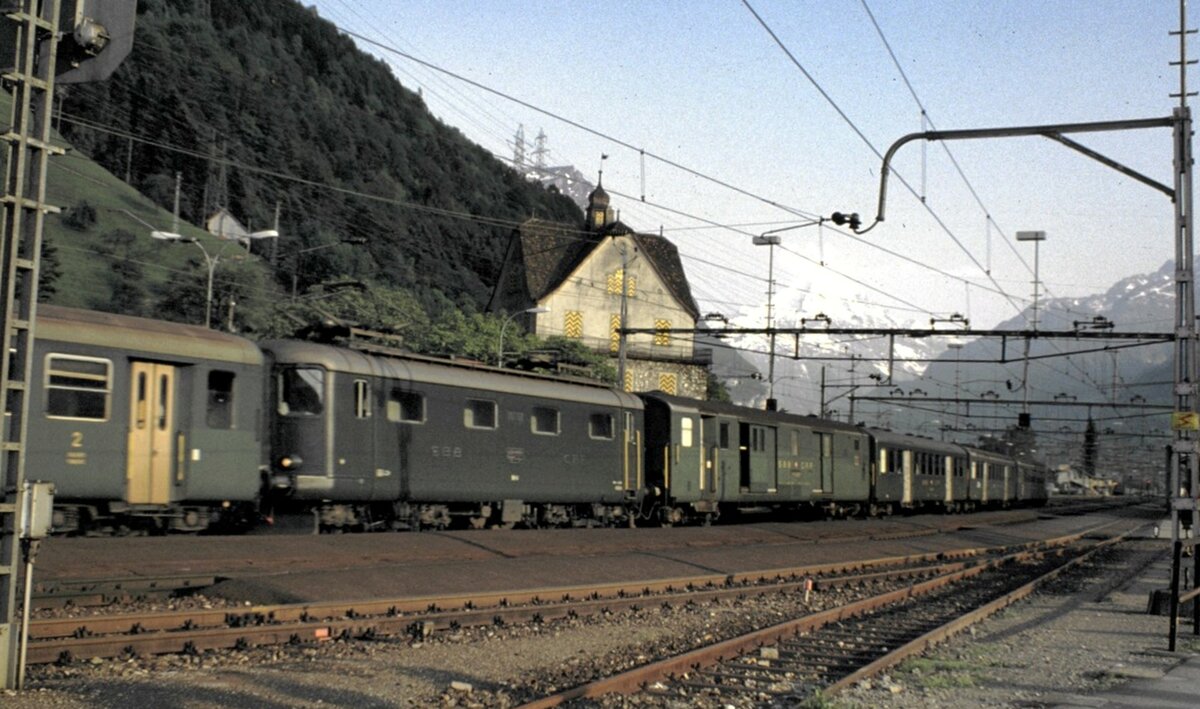 SBB Re 4/4 I im Zugverband in Flüelen am 30.05.1981. Einige Re 4/4 I der ersten Serie hatten in der Front Türen und auf einer Seite einen abgeschirmten Gang, der auf diesem Foto erkennbar ist. So konnte vom vorderen in den hinteren Teil durch die Lok gelangt werden (oder in umgekehrter Richtung).