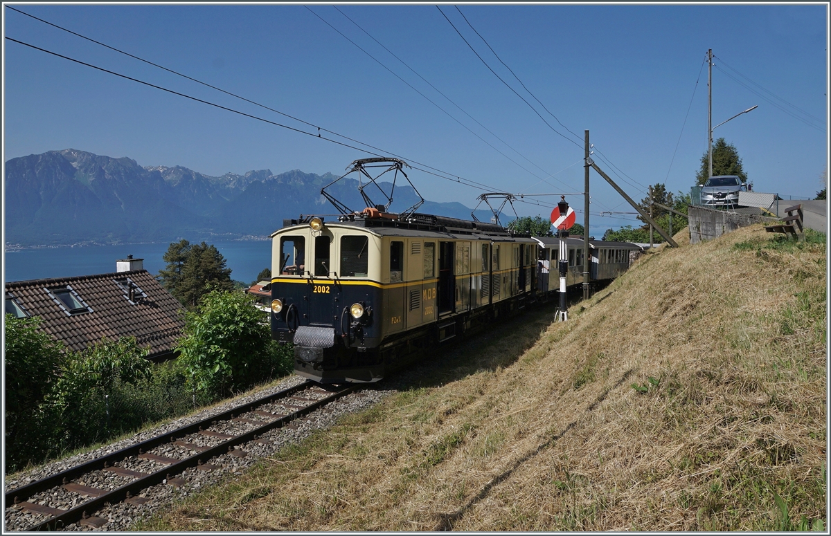 Zugunsten der Aussicht wählte ich hier die Schattenseite des Zuges, welcher der MOB DZe 6/6 2002 kurz nach Blonay in Richtung Chamby zieht. Im Hintergrund rechts des Zuges ist das Einfahrsignal von Blonay zu erkennen, eine Hippsche Wendescheibe, genannt nach seinem Erbauer, dem Elektriker und Uhrenmacher Matthäus Hipp, geboren in Blaubeuren (1813), der dann beruflich in der Schweiz tätig war. 
Der Blick gleitet des weitern weit über den Genfersee zu den Savoyer Alpen. 

4. Juni 2022