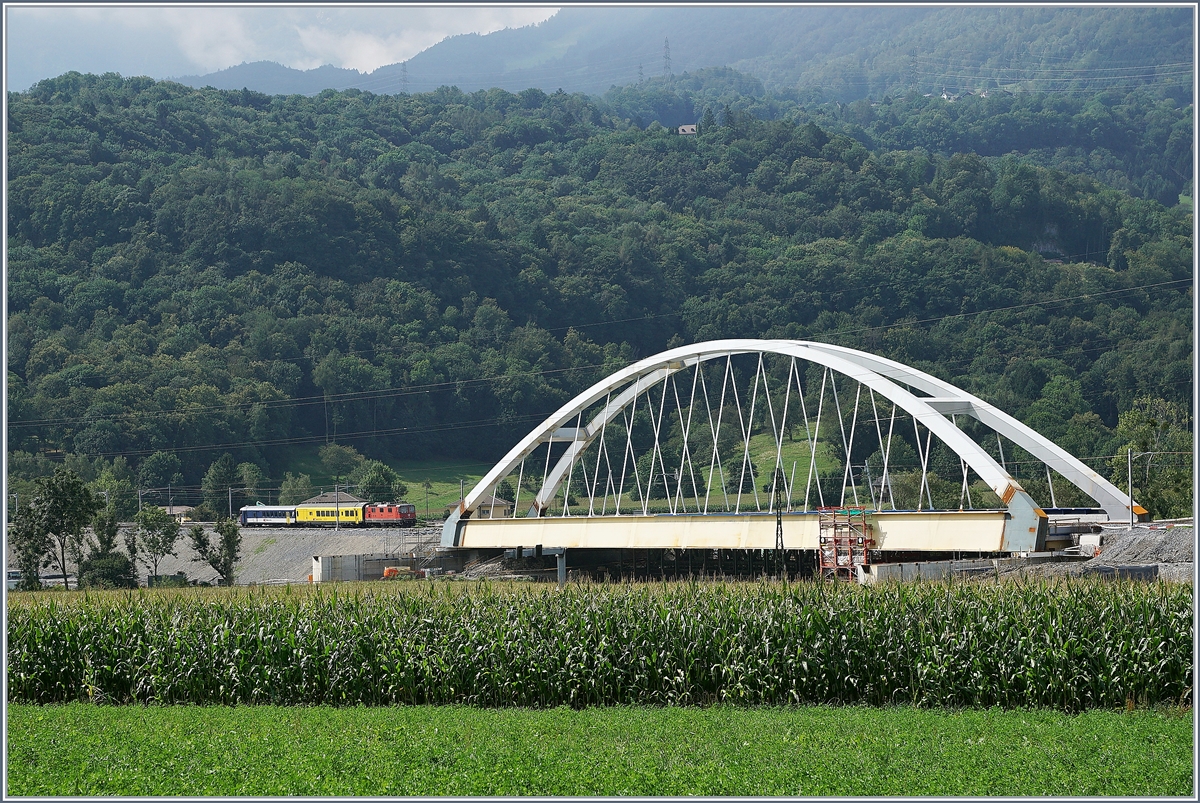 Zwischen Bex und St-Maurice überquert die Strecke Lausanne Birg die Rhone. Die alte Gittereisenbrücke wird nun durch eine sehr gefällige und unübersehbare Neukonstruktion ersetzt. Zu Zeit ist die alte Brücke schon nicht mir in Betrieb und der Verkehr verläuft einspurig über die neue Brücke, wobei vor und nach der Brücke das nördliche Gleis, dann auf der Brücke das Südliche Gleis benutzt wird, so dass die Brücke noch verschoben werden muss. Leider ist es nicht einfach, einen einigermasen guten Fotostandpunkt zu finden.
Auf dem Bild links der Brücke: eine SBB Re 4/4 II mit einem Messzug auf der Fahrt Richtung St-Maurice.
19. August 2016