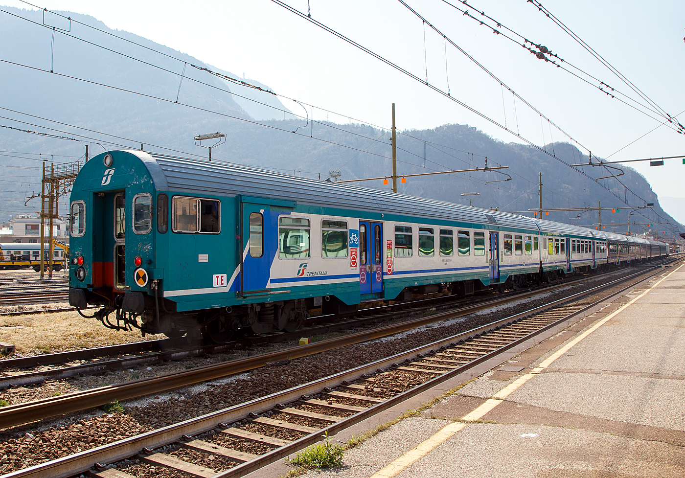 2. Klasse Reisezug- MDVC-Steuerwagen mit Gepäckabteil (MDVC steht für Medie Distanze Vestiboli Centrali, deutsch für Mittlere Entfernungen in Ballungsräumen) 50 83 82-86 807-5 I-TI der Trenitalia, der Gattung npBD und Bauart APR ( Hasenkasten -Steuerwagen) am 26.03.2022 im Bahnhof Bozen / Bolzano.

Die den Wagen handelt es sich um in Italien hergestellte Eisenbahnwaggons die speziell für den Einsatz für mittlere Entfernungen wie z.B. RE (Regionalexpress Züge). Das „TE“ (vorne unten zeigt das es sich um einen Steuerwagen vom Typ TE (Tipo TE) für E-Loks handelt.

TECHNISCHE DATEN:
Spurweite: 1.435 mm
Länge über Puffer: 26.400 mm
Breite: 2.825 mm
Höhe: 3.965 mm
Drehzapfenabstand: 19.000 mm
Achsstand im Drehgestell: 2.400 mm
Laufraddurchmesser : 860 mm (neu)
Fußbodenhöhe: 1090 mm
Eigengewicht: 40 t
Sitzplätze: 60 (2. Klasse)
Zuladegewicht: 3 t
Höchstgeschwindigkeit: 160 km/h
Bremsbauart: Freno WU-R