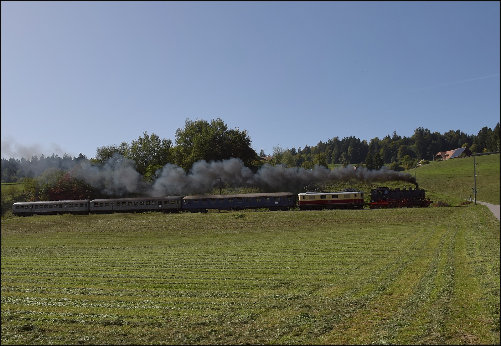 Dampftage Huttwil mit frisch genesenem Bubikopf. 

In Griesbachmatten geht es für 64 518 und Re 4/4 I 10034 die steile Rampe nach Weier hinauf. Oktober 2023.