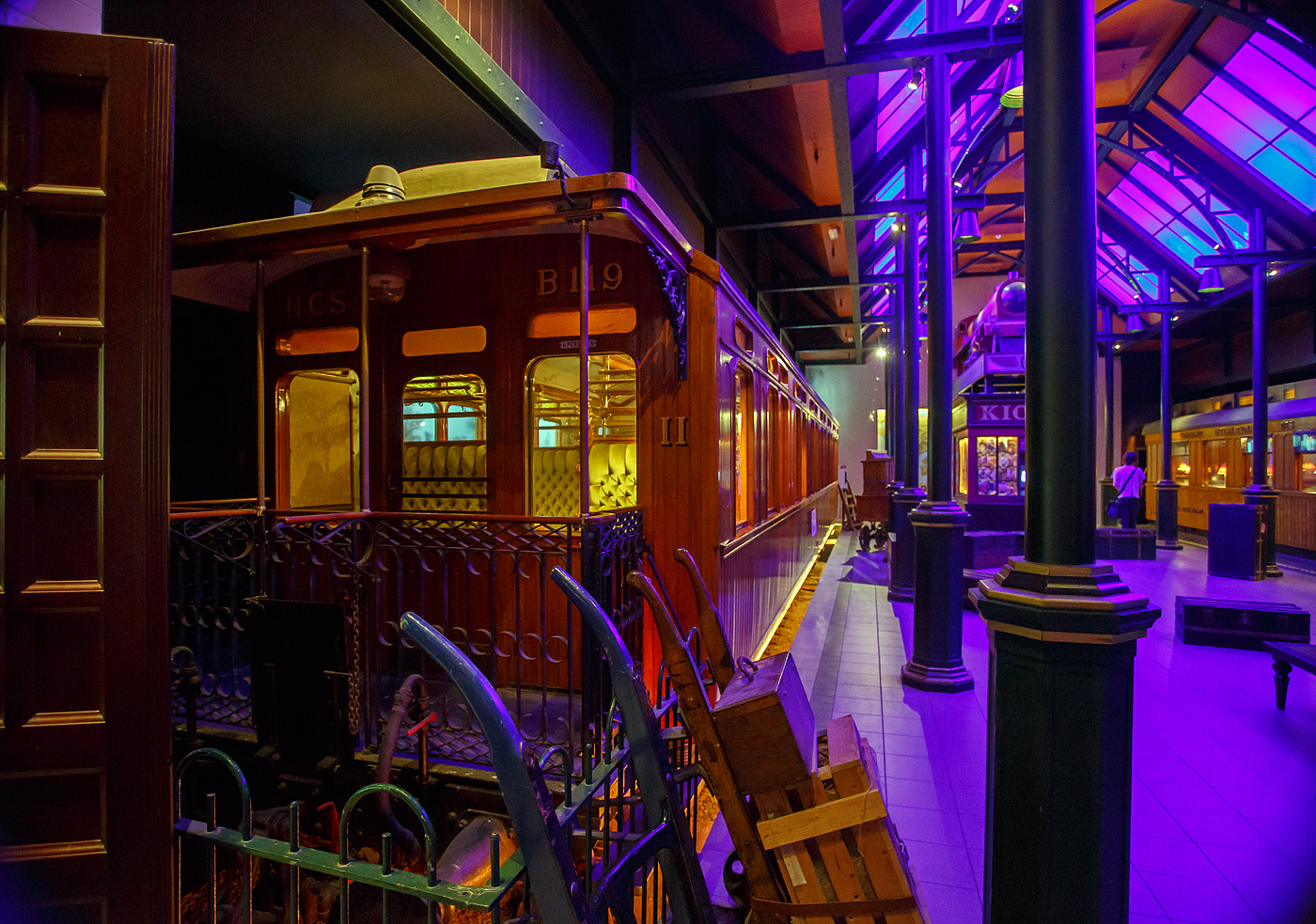 Der zweite Klasse Reisezugwagen NCS B 119, ein luxuriöser Teakholzwagen der ehemaligen NCS - Nederlandsche Centraal Spoorwegmaatschappij (Niederländische Zentralbahngesellschaft) am 24. Juni 2025 im Het Spoorwegmuseum (bis 2005 NSM - Nederlands Spoorwegmuseum / Niederländischen Eisenbahnmuseum) in Utrecht im ehemaligen Bahnhof Maliebaan. Nicht nur die Compagnie Internationale des Wagons-Lits (CIWL) für ihre Luxuszüg, wie beispielsweise dem Orient-Express, hatte solche Wagen.

Dieser äußerst luxuriösen Abteilwagen vom Typ BL8 (Serie B 111 – 127) wurde 1904 in der eigenen Werkstatt der NCS in Utrecht (Werkplaats NCS) gebaut. 

Bedingt durch den Ersten Weltkrieg wurde 1917 eine Zweckgemeinschaft der unabhängigen Eisenbahngesellschaften HSM beziehungsweise HIJSM (Hollandsche IJzeren Spoorweg-Maatschappij) und SS (Maatschappij tot Exploitatie van Staatsspoorwegen) gegründet. Da die NCS unter der Kontrolle der SS stand, wurde sie von diesem Moment an auch Teil der neuen Partnerschaft. Der Betrieb wurde am 1. Juni 1919 an die SS übertragen. Die beiden Gesellschaften errichteten einen gemeinsamen Bahnbetrieb, blieben aber rechtlich unabhängig. Dies änderte sich 1938, als HIJSM und SS vollständig fusionierten und in der AG NS (Nederlandse Spoorwegen, früher Nederlandsche Spoorwegen geschrieben) aufgingen. Das Rollmaterial wurde bereits 1921 zusammengelegt. Somit wurde ab 1924 der Wagen als NS B 1814 geführt, 1952 wurde er außer Dienst gestellt und für das Eisenbahnmuseum erhalten. Er kam 1977 vollständig restauriert als NCS B 119 dort an. Seitdem ist ein Paradewagen des Museums.

Anfang des 20. Jahrhundert war es den lokalen Eisenbahnen in den Niederladen gesetzlich verboten Waggons der 1. Klasse einzusetzen. Um doch wohlhabende Passagiere von Zeist und Baarn (einschließlich des Direktors der NCS) in passender Art zu befördern umging die NCS mit diesen als 2. Klasse Wagen klassifizierten äußerst luxuriösen Standard. Neben den teakholzgetäfelten Außenwänden ist auch der Innenraum opulent und gepflegt. Zu beiden Seiten des Mittelgangs befinden sich gepolsterte Doppelbänke mit Wendekissen. Im Winter war die plüschige Seite oben, im Sommer die kühlere, lederbezogene Seite. Lampen, Gepäckablagen, Aschenbecher, alles ist wunderschön verarbeitet und aus Kupfer gefertigt. Die Waggons wurden unter anderem auf den (Lokal-)Bahnen Utrecht–Den Dolder–Baarn und Utrecht–Bilthoven–Zeist eingesetzt. Insgesamt gab es siebzehn dieser Wagen.

TECHNISCHE DATEN:
Baujahr: 1904 (Ausmusterung 1952)
Spurweite: 1.435 mm (Normalspur)
Achsen: 4 (in 2 Drehgestellen)
Achsfolge: 2'2'
Länge über Puffer: 17.540 mm
Höchstgeschwindigkeit: 80 km/h
Sitzplätze: 56 in 8 Abteilen
