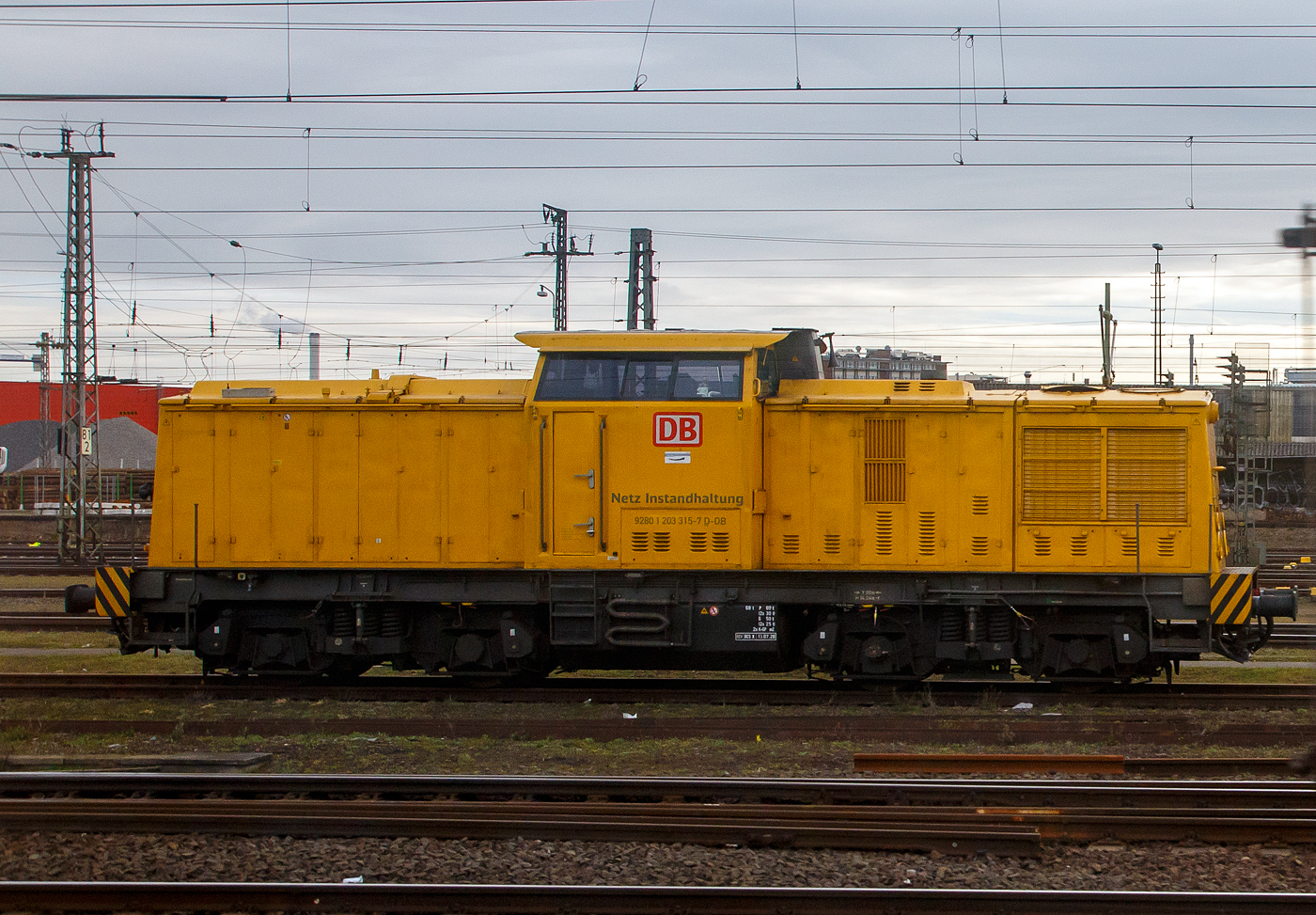 Die 203 315-7 (92 80 1203 315-7 D-DB) der DB Netz AG steht am 21.03.2023 bei Frankfurt am Main (aus einem Zug heraus fotografiert).

Die V 100.1 wurde 1973 bei LEW (VEB Lokomotivbau Elektrotechnische Werke „Hans Beimler“, Hennigsdorf) unter der Fabriknummer 13943 gebaut und als 110 625-1an die DR ausgeliefert.

Weiterer Lebenslauf:
1983  Umbau Bw Karl-Marx-Stadt  in DR 112 625-9
01.01.1992 Umzeichnung in DR 202 625-0
01.01.1994 DB  202 625-0
2002  an ALS - ALSTOM Lokomotiven Service GmbH (Stendal) hier erhielt sie einen neuen CAT-Motor und wurde entsprechend in 203 315-7 umbezeichnet.
2003  an DB Bahnbau GmbH
Und seit 2004 bei der DB Netz AG