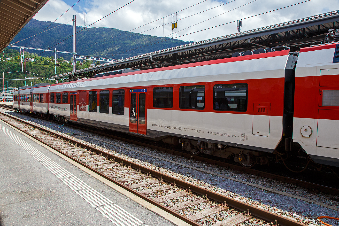 Die relativ vierachsige INOVA-Zwischenwagen mit Niederfluranteil fr die NPZ Domino-Zge (RBe 560), gebaut 2008 bis 2009 durch Bombardier in Villeneuve. Hier der Wagen B NPZ DO RA 50 85 29-43 407-0 CH-RA der RegionAlps, eingereiht in den RA 12 (RBDe 560 412-9) am 25.05.2023 im Bahnhof Brig. Die Wagen der  RegionAlps SA tragen den Werbespruch fr die Region auf Deutsch und Franzsisch (Wallis, in mein Herz eingebrannt / Valais, Grav dans mon coeur). Die Wagen haben ein rollstuhlgngiges und damit behindertengerechtes WC erhalten.

TECHNISCHE DATEN:
Spurweite:  1.435 mm (Normalspur)
Anzahl der Achsen: 4
Lnge ber Puffer:  24.700 mm 
Drehzapfenabstand: 18.900 mm 
Achsabstand im Drehgestell: 2.500 mm
Gewicht:  36 t 
Hchstgeschwindigkeit: 140 km/h
Sitzpltze: 60

Die Regionalps (RA) ist ein Eisenbahnverkehrsunternehmen im Kanton Wallis, mit Sitz in Martigny hat. Eigentmer derim Jahr 2003 gegrndete Gesellschaft  sind die Schweizerischen Bundesbahnen (SBB) mit 70 %, die Transports de Martigny et Rgions (TMR) mit 18 % und der Kanton Wallis mit 12 %. Die RA betreibt den Regionalverkehr vor allem im Rhonetal zwischen dem Ostufer des Genfersees und Brig. Inzwischen gehren Regionalps 16 dreiteilige NPZ Domino (Trieb-, Zwischen- und Steuerwagen ex SBB) und 4 RABe 525 NINA (ex TMR).