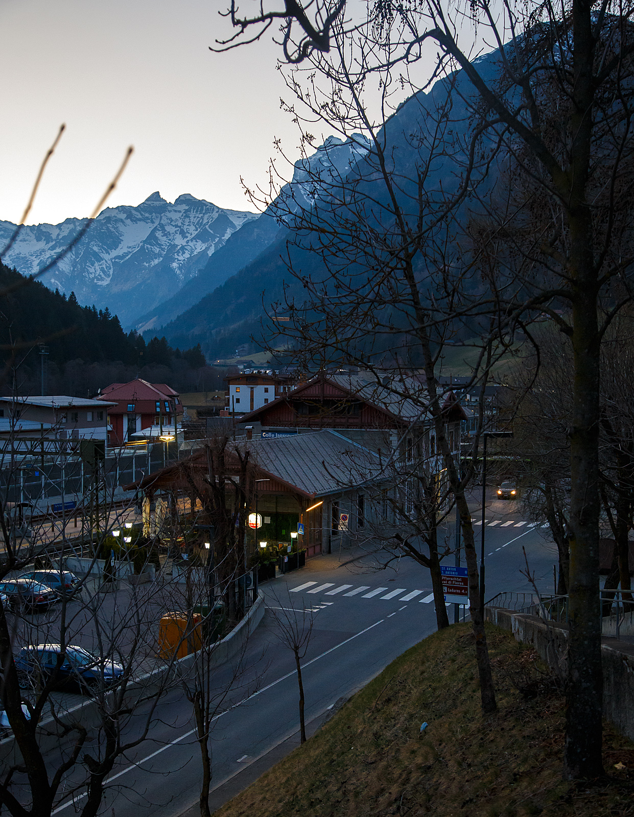 Ein abendlicher Blick auf den Bahnhof Gossensaß/Colle Isarco am 26.03.2022.
Der Bahnhof Gossensaß (auch Gossensass; italienisch Stazione di Colle Isarco) befindet sich an der Brennerbahn in Südtirol (italienisch Alto Adige), amtlich Autonome Provinz Bozen – Südtirol.

Der Bahnhof Gossensaß ist der erste Haltepunkt im Wipptal südlich des Brennerpasses, zu dem die Bahnstrecke von hier aus über den Pflerschtunnel ansteigt. Er liegt auf 1.066,9 m Höhe nahe dem Zentrum von Gossensaß, dem Hauptort der Gemeinde Brenner, und der durch das Dorf führenden SS 12 (der alten Brennerpass-Straße). 

Der Bahnhof wurde 1867 zusammen mit dem gesamten Abschnitt der Brennerbahn zwischen Innsbruck und Bozen in Betrieb genommen. Durch ihn erlebte Gossensaß bis zum Ersten Weltkrieg seine Blütezeit als bekannter Touristenort. Er konkurrierte mit Orten wie St. Moritz oder Chamonix. 

Das Aufnahmegebäude war zunächst noch relativ kompakt gehalten, wurde wegen der vielen Touristen jedoch noch im 19. Jahrhundert durch einen südlichen Anbau erweitert. Das ursprüngliche Gebäude weist eine Verkleidung aus Grauwacke auf, während dekorative Details wie die Fensterfassungen in weißem Kalkstein gehalten sind. Straßenseitig ist es durch einen in sorgfältigen Details gearbeiteten Dachgiebel aus Holz gestaltet. Der Anbau ist in Brixner Granit gemauert und sticht durch eine hölzerne Veranda hervor. In dem sich heute das Buffet befindet und man auch den Espresso genießen kann. Das Gebäude steht seit dem Jahr 2000 unter Denkmalschutz.

Der Bahnhof Gossensaß wird durch Regionalzüge der Trenitalia sowie der SAD bedient, die auch Busverbindungen zum Bahnhof betreibt. Die Regionalzüge fahren in beide Richtung (Brenner bzw. Bozen) im Stundentakt und werden zu Hauptverkehrszeiten durch Regionalexpresszüge verdichtet.

Uns hat es in Gossensaß sehr gut gefallen, es war einfach zu kurz, so dass wir gerne wiedermal dort hinfahren wollen. Für die drei Tage haben wir uns ein Südtirol/Alto Adige Ticket (eine Mobilcard für 3 Tage) am Automat für 23,00 Euro geholt. So konnten wir mit diesem Ticket Südtirol mit der Bahn erkunden. 