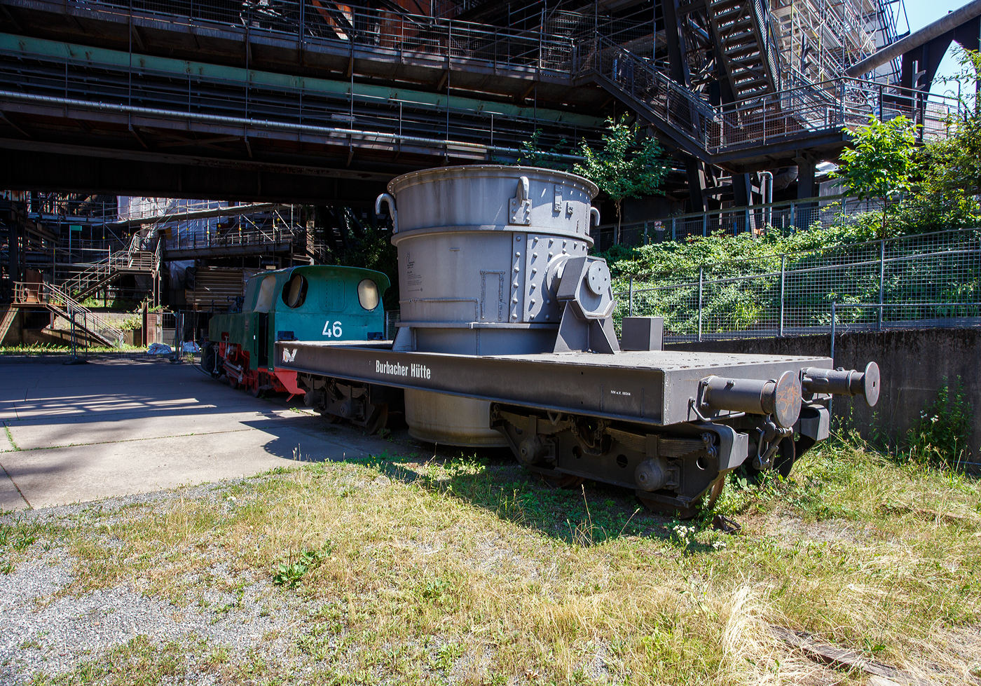 Ein vierachsiger normalspuriger offener Roheisenpfannenwagen der Burbacher Htte hinter der Normalspur-Dampflokomotive 46, einer Jung Hochofenlok niedriger Bauart, der Vlklinger Htte (ehem. Rchling'schen Eisen- und Stahlwerke GmbH in Vlklingen/Saar, ab 1982 ARBED-Saarstahl GmbH, ab 1986 Saarstahl Vlklingen GmbH), ausgestellt als Denkmal am Gelnde Vlklinger Htte, hier am 01 Juli 2025 am Gelnde Vlklinger Htte als Denkmal. Heutiger Eigentmer ist die Initiative Vlklinger Htte e.V..

1971 fusionierten die Burbacher und Vlklinger Htte, und ab 1975 wurde die Stahlproduktion in der Burbacher Htte eingestellt. Das Bild zeigt einen offenen Pfannenwagen, mit dem das flssige und heie Roheisen aus dem Hochofen aufgefangen wird, und dann zur Weiterverarbeitung mittels Werkseisenbahn zur Weiterverarbeitung in das angrenzende Stahl- und Walzwerk weitertransportiert wurde. Da die Entfernungen gering waren, bentigte man keine mit Schamott ausgemauerten Torpedopfannenwagen. Ob der Wagen hier auf der Vlklinger Htte ist mit nicht klar, aber da er erheblich hher ist als die Lok, so vermute ich das er hier keinen Einsatz fand.