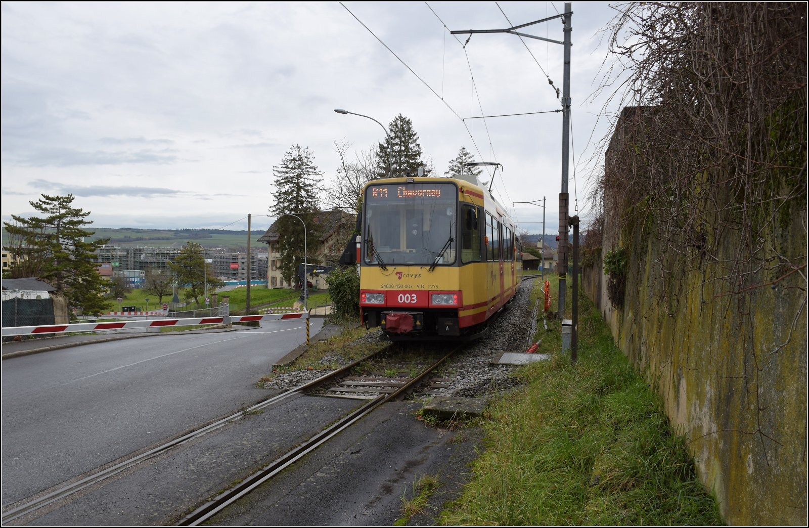 Ende einer �ra - der Gleichstrom und die  Lokalbahn  gehen. 

Ausfahrt der Karlsruher Zweisystem-Strassenbahn  Be 4/8 003  alias 94 800 450 003-9 D-TVYS aus St. Eloi. Die Platzverh�ltnisse sind hier deutlich beengt, den an den Bahn�bergang reihen sich nach hinten Bahnsteig und Orbe-Br�cke. Orbe, Dezember 2025.