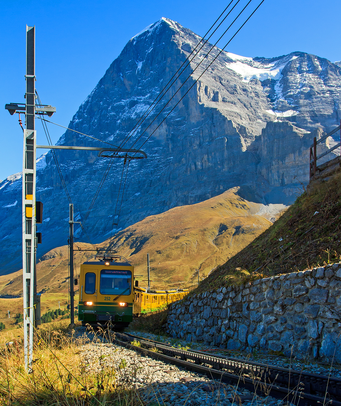 Geführt vom sechsachsigen Gelenksteuerwagen Bt 252 erreicht der WAB – Wengernalpbahn Zug von Grindelwald kommend am 02.10.2011 die Kleine Scheidegg.

Im Hintergrund die berühmte Eiger Nordwand.
