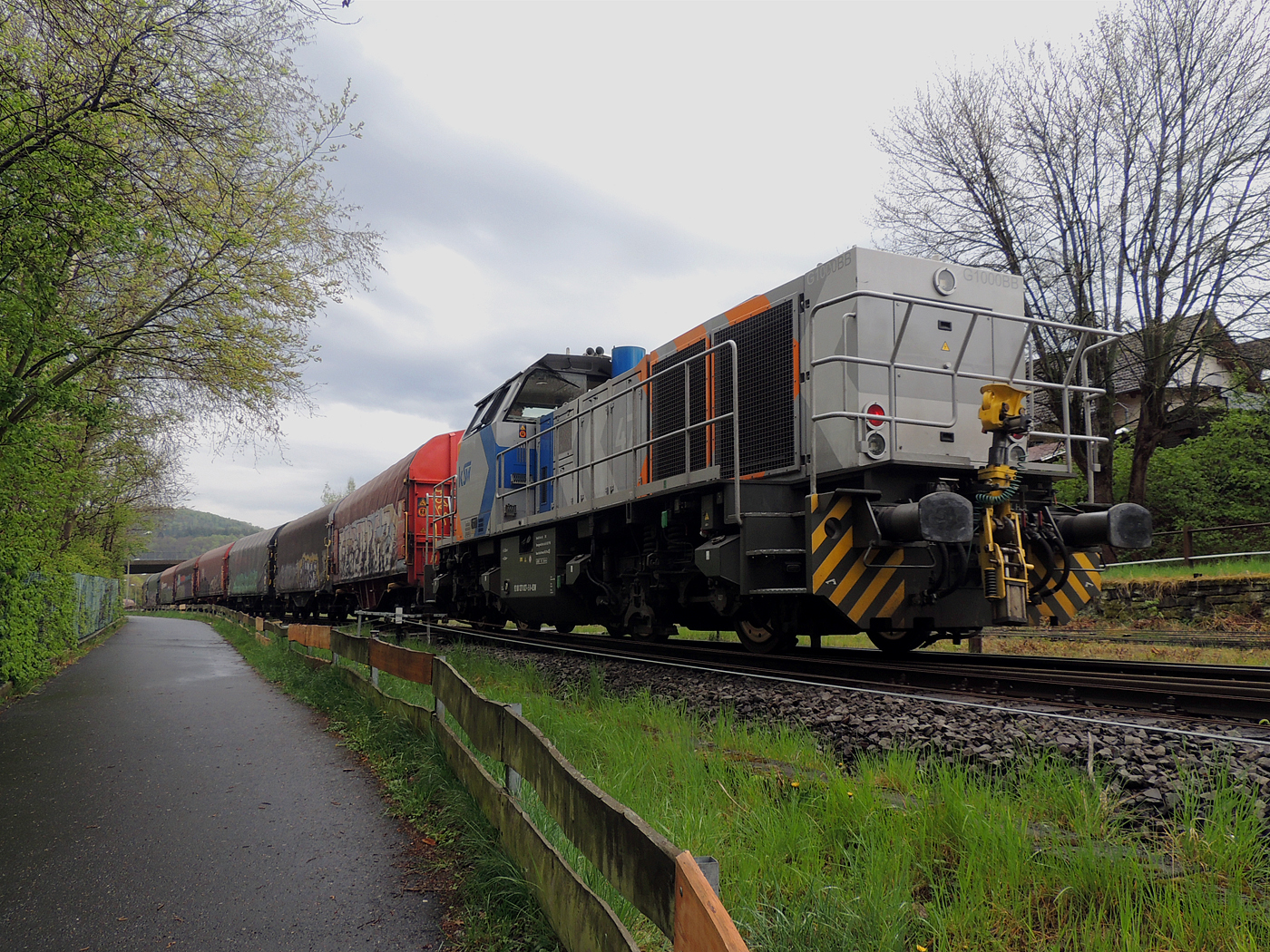 Hochbetrieb in Herdorf am 23 April 2025: 
Durch die vergangenen Osterfeiertage braucht es wohl wieder Nachschub. Die KSW (Kreisbahn Siegen-Wittgenstein) kommt im Sandwich mit einem sehr langen und somit schweren Coilzug, von via Betzdorf/Sieg kommend, und erreicht den KSW-Rangierbahnhof (Betriebsstätte FGE - Freien Grunder Eisenbahn).

Hier am Zugschluss die nachschiebende KSW 47 (92 80 1271 027-5 D-KSW), ex D 2 der HFM, eine Vossloh G 1000 BB, vorne als Zuglok die KSW 44 (92 80 1271 004-4 D-KSW) auch eine MaK G 1000 BB. Im Rbf wird der Zug geteilt, da er für die Weiterfahrt sonst zu lang wäre, und die KSW 44 zieht den ersten Teil weiter zu den Schäfer Werke KG am Pfannenberg in Neunkirchen-Salchendorf. 

Die KSW-Bahnstrecke Herdorf–Pfannenberg-(ehem. Unterwilden) ist eine rund 8 km lange Nebenbahn, bekannt ist sie auch als „Talbahn“. Die Strecke wurde von der 1904 gegründeten Freien Grunder Eisenbahn AG betrieben. Die gebliebenen Gleise und Anlagen sind seit 1970, als Betriebsstätte FGE - Freien Grunder Eisenbahn. Teil der heutigen Kreisbahn Siegen-Wittgenstein.

Später kam dann noch die KSW 43 (92 80 1273 018-2 D-KSW), die asymmetrische Vossloh G 2000 BB, mit einem langen Coilzug von Duisburg an.