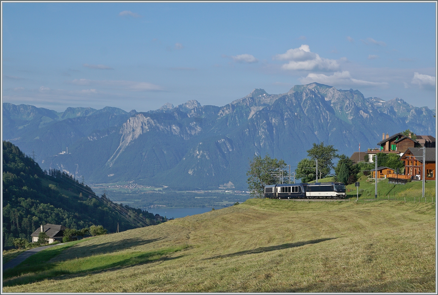 Mit Blick auf Walliser und Savoyer Alpen sowie den Genfersee als Bildhintergrund, erscheint die MOB Ge 4/4 8002 mit dem Golden Pass Express GEX 4064 von Montreux nach Interlaken Ost bei Les Avants. In Zweisimmen wird eine BLS Re 465 die MOB ge 4/4 8002 ablösen. 

28. Juni 2024