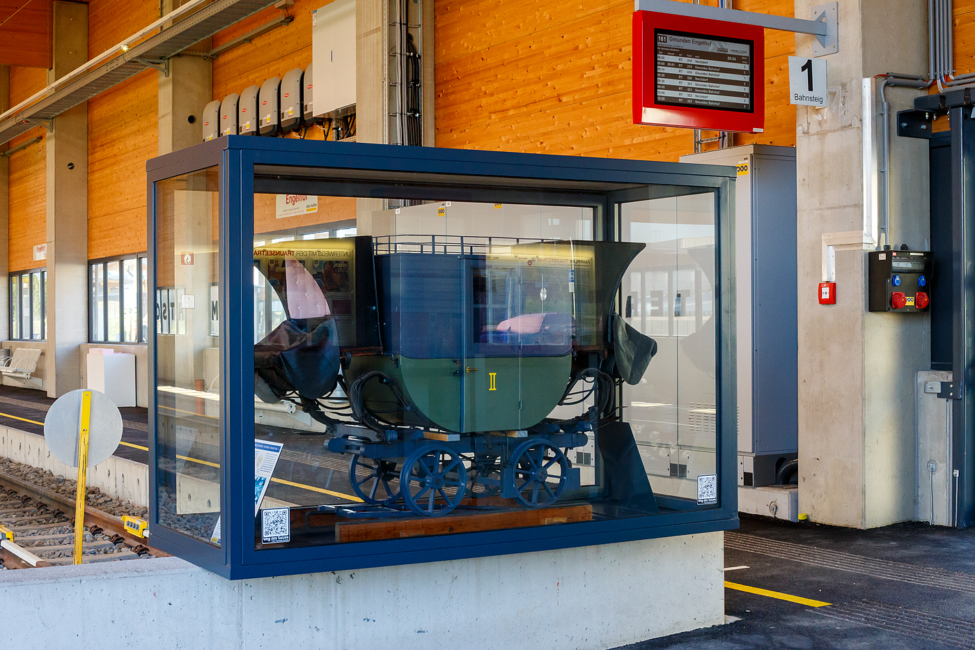 Nein keine Postkusche, sondern ein Modell von einem Personenwagen der 2. Klasse  Hannibal  der der Budweis-Linz-Gmundener Pferdeeisenbahn, hier auf einem Schleppwechsel (Weiche) dieser Bahn stehend. Ausgestellt im Bahnhof Engelhof der Traunseetram (Lokalbahn Gmunden–Vorchdorf), hier am 04 April 2025. 

Das heute noch erhaltene Bahnhofsgebäude Engelhof hat von 1836 bis 1855 als Stationsplatz Englhof mit Pferdeställen der Pferdeeisenbahn gedient. Nach 1855 wurde der Bahnhof von der inzwischen längst eingestellten Linie Gmunden–Laakirchen–Lambach genutzt. Heute nutzt ihn noch die Traunseebahn (Lokalbahn Gmunden–Vorchdorf) als Bahnhof. Der denkmalgeschützte Bahnhof Engelhof ist der älteste noch in Funktion stehende Bahnhof Kontinentaleuropas!

Ein erhaltenes Original von einem dieser 1941 in Linz-Urfahr gebauten Hannibal-Waggon steht heute im Technischen Museum Wien. Mit der Einstellung der Linz Budweiser Pferdeeisenbahn am 15. Dezember 1872 wurde der Wagen außer Verwendung gesetzt. Ursprünglich war es ein 1. Klasse Wagen, mit der Umstellung der Südstrecke von Linz nach Gmunden auf Dampfbetrieb in Jahr 1855, und der Anschaffung neuer und komfortablerer Personenwagen, wurden die alten Pferdebahnwagen zur 2. Klasse umgezeichnet. Nach Einstellung der Pferdeeisenbahn 1872, war  Hannibal  ein Glanzstück der Ausstellung über die Verkehrsgeschichte auf der Wiener Weltausstellung 1873. Danach geriet er in einem Schuppen im Prater in Vergessenheit. Nach der Wiener Gewerbeausstellung 1888, wurde er zerlegt am Dachboden der Werkstätten am Westbahnhof gelagert. Dort gingen einige Teile verloren. 1893 fand er einen neuen Platz im k.k. historischen Museums der Österreichischen Staatsbahnen.

Bereits seit Achttausend Jahren wird im Salzkammergut Salz abgebaut und das abgebaute Salz wurde, über 1000 Jahre lang über die Traun (Fluß) befördert. Der Salztransport entlang der Traun, war nicht nur gefährlich, sondern auch teuer. Demnach war der Bau der Pferdeeisenbahn plausibel. Im Jahre 1834 begannen die ersten Bauarbeiten der südlichen Strecke von Linz nach Gmunden, welche bereits nach zwei Jahren abgeschlossen wurden. So war nun die komplette Strecke der Pferdeeisenbahn Budweis–Linz–Gmunden fertig. Sie war nach der 1827 eröffneten Bahnstrecke Saint-Étienne–Andrézieux, die zweite öffentliche Eisenbahnlinie auf dem europäischen Festland und diente hauptsächlich dem Transport von Salz aus dem oberösterreichischen Salzkammergut nach Böhmen (was ja bis 1918 zur Habsburgermonarchie gehörte). 

Die Strecke war in der ungewöhnlichen Spurweite von 1.106 mm (3 österr. Fuß 6 Zoll) ausgeführt. Es waren aber keine Eisenschienen auf denen die Spurkranzräder liefen, sondern Holzschienen (Balken) auf denen Flacheisen mit handgefertigten Nägeln befestigt waren. Die Streckenlänge betrug von Budweis nach Linz 128,8 km und von Linz nach Gmunden 67,9 km, somit fast 200 km. Die Trasse war eingleisig mit zahlreichen Ausweichen ausgeführt.

Die Bahngesellschaft besaß ca. 1000 Güterwagen. Das Ladegewicht betrug 2,5-3,3 t. Zur Beförderung der Fracht verwendete man offene und gedeckte Wagen. Die Hauptfracht Salz wurde mit zweiachsigen, offenen Niederbordwagen, auf denen man rund 40 Fässer mit je 56 kg laden konnte, befördert. Einige Wagen waren für den Kohle-, Steine- und Langholztransport vierachsig. Die Personenwagen wiesen verschiedene Bauarten auf, es gab offene und gedeckte Wagen und hatten bis zu 24 Sitzplätze. Die Wagen waren in drei Klassen unterteilt und trugen Namen.

Gezogen wurden die Wagen meist von einem Pferd, bei steigungsreichen Abschnitten wurde ein zweites Pferd vorgespannt. Zugpferde waren so gut wie ausschließlich Noriker. Der Noriker (auch Pinzgauer) ist ein mittelschweres, kräftiges und ausdauerndes Gebirgskaltblutpferd, die sich als stark und genügsam erwiesen. Die Gesellschaft verfügt im Vollbetrieb über 600 Pferde. Die Geschwindigkeit der Güterzüge betrug im Schnitt 4 km/h, pro Tag wurden maximal 40 Kilometer zurückgelegt. So brauchte ein Güterwagen von Gmunden nach Budweis 5 Tage.

Die Strecke zwischen Linz und Gmunden wurde in den Jahren 1855 und 1856 auf Dampfbetrieb umgestellt. Auf der gebirgigen Strecke zwischen Linz und Budweis (České Budějovice) war diese Umstellung aufgrund zu enger Krümmungsradien und zu großer Steigungen nicht möglich. Bis 1873 wurden daher als Ersatz die Bahnstrecken Linz–Gaisbach-Wartberg und St. Valentin–České Budějovice mit zumeist anderer Trassenführung zwischen Linz und Budweis errichtet, die den Dampfbetrieb zuließ. Der Pferdebahnbetrieb wurde im Dezember 1872 eingestellt.