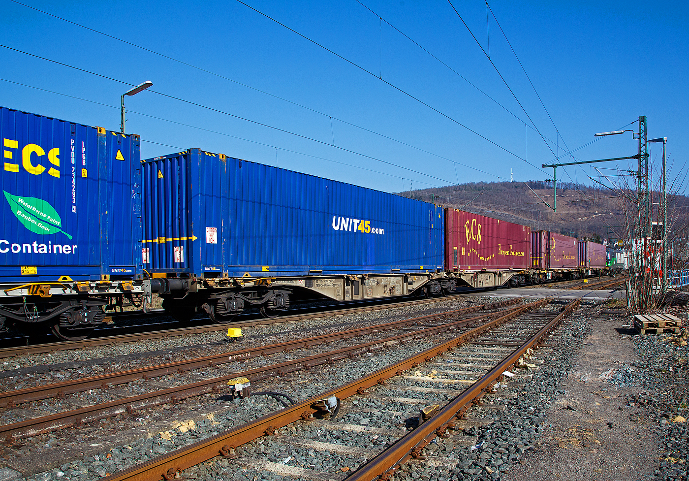 Sechsachsiger Drehgestell-Gelenk-Containertragwageneinheit 90´, 33 85 4961 290-5 CH-HUPAC der Gattung Sggmrss 90`der HUPAC AG am 24.03.2021 im Zugverband bei der Durchfahrt in Niederschelden an der Siegstrecke (KBS 460) in Richtung Siegen.

Diese Gelenkwagen mit sechs Radsätzen sind für den Transport von Großcontainern und Wechselbehältern vorgesehen. Auf den Außenlangträger des Wagens befinden sich für jede vorgesehene Ladeposition feste und klappbare Aufsetzzapfen zum Festlegen der Ladungseinheiten (gemäß UIC- Merkblatt 592-1 und 2) in verschiedenen Kombinationen.

Das aus zwei Wagenhälften bestehende Untergestell ist eine verwindungsweiche, geschweißte Rahmenkonstruktion aus Walz- und Blechprofilen, gebildet aus den Kopfstücken, den Hauptquerträgern und den äußeren Langträgern. In der Wagenmitte befindet sich eine Übersteigmöglichkeit.

TECHNISCHE DATEN:
Spurweite: 1.435 mm
Länge über Puffer: 29.590 mm
Drehzapfenabstand: 2 x 11.995 mm
Achsabstand in den Drehgestellen: 1.800 mm
Drehgestelle: 3 x Y25Lss1-K
Laufraddurchmesser: 920 mm (neu)
Ladelänge: 2 x 13.820 mm
Höhe der Ladeebene über S.O.: 1.155 mm
Eigengewicht: 27.400 kg
Max. Zuladung bei Lastgrenze S: 107,6 t (ab Streckenklasse D)
Max. Zuladung bei Lastgrenze SS: 92,6 t (ab Streckenklasse C)
Max. Geschwindigkeit: 100 km/h (Lastgrenze SS und leer 120 km/h)
Kleinster befahrbarer Gleisbogen: R 75 m 
Bremse: 2 x KE-GP-A 
Bremssohle: Jurid 816M
Feststellbremse: Ja
Verwendungsfähigkeit: TEN GE