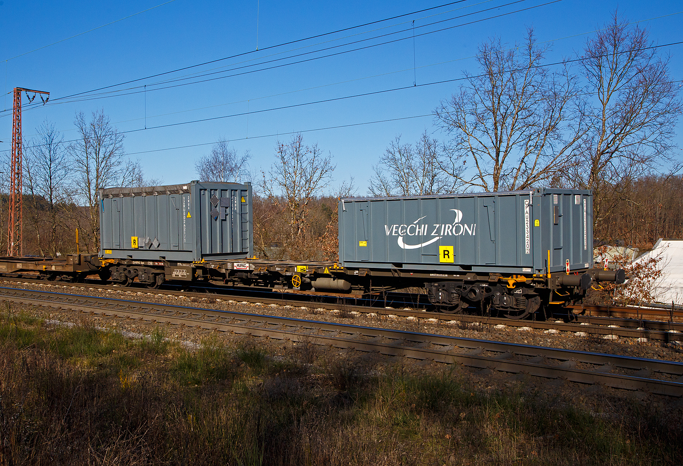 Vierachsiger Drehgestell-Containertragwagen der Gattung Sgns, 33 85 4555 518-8 CH-HUPAC, der HUPAC SA, am 07.02.2023 im Zugverband bei der Durchfahrt in Rudersdorf (Kr. Siegen) in Richtung Siegen.

Bedeutung der Gattung Sgns:
S   Drehgestell-Flachwagen in Sonderbauart
g   Für Container mit einer Gesamtlänge von höchstens 60 Fuß
n   Maximale Tragfähigkeit über 60 t
s   Höchstgeschwindigkeit 100 km/h (beladen)

TECHNISCHE DATEN:
Spurweite: 1.435 mm
Länge über Puffer: 19.640 mm
Drehzapfenabstand: 14.200 mm
Achsabstand in den Drehgestellen: 1.800 mm
Eigengewicht: 20.000 kg
Max. Zuladung: 70,0 t (ab Streckenklasse D)
Max. Geschwindigkeit: 100 km/h (beladen) / 120 km/h (leer)
Kleinster befahrbarer Gleisbogen: R 75 m 
Bremse: Frein 0-GP-A