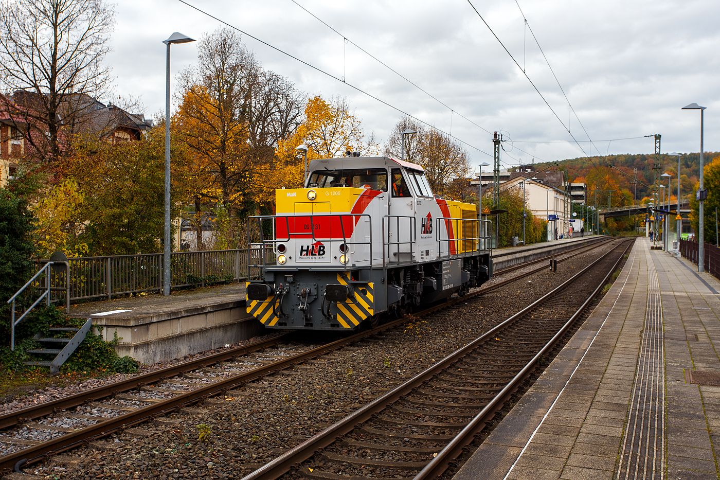 Welch seltener Gast auf der Siegstecke, auch wenn Triebzüge und -wagen der HLB hier Alltag sind, ist die Güterlok der HLB meist in und um Kassel unterwegs. Die Diesellokomotive 275 024-8, alias DG 1131 (92 80 1275 024-8 D-HEB), die Vossloh/MaK G 1206 der HLB - Hessische Landesbahn GmbH, hat am 16 Oktober 2025, auf den Weg in Richtung Köln, im Bahnhof Kirchen/Sieg Hp 0, da es eine Weichenstörung gab.

Die MaK G 1206 wurde 2001 von der VSFT - Vossloh Schienenfahrzeugtechnik GmbH in Kiel-Friedrichsort unter der Fabriknummer 1001131 gebaut und an die LC - Locomotion Capital Ltd. (London) als Mietlok geliefert. 

Lebenslauf/Stationen und Bezeichnungen:
•	Dezember 2001 - Vermietung an NE - Städtische Hafenbetriebe Neuss
•	Januar 2002 - Vermietung an StEK - Städtische Eisenbahn Krefeld 
•	Januar 2002 - Vermietung an Niederrheinische Verkehrsbetriebe AG (NIAG) 
•	Januar/Februar 2002 - Vermietung an OHE- Osthavelländische Eisenbahn AG 
•	Februar 2002 bis August 2003 - Vermietung an IL - InfraLeuna Infrastruktur- und Service GmbH, als IL 206
•	April 2003 - Verkauf an ATC - Angel Trains Cargo SA, Antwerpen (B)
•	August 2003 bis - Vermietung an RBH - RAG Bahn und Hafen GmbH als  RBH 841  
•	April bis Juni 2005 - Vermietung an MEG - Mitteldeutsche Eisenbahn GmbH  MEG 298  
•	November 2005 bis Oktober 2006 - Vermietung an MVG - Mülheimer Verkehrsgesellschaft mbH, Mülheim (Ruhr)  2  
•	November 2006 bis 2013 Vermietung an CFL - Société Nationale des Chemins de Fer Luxembourgeois bzw. CFL Cargo als 1504. Ab 2007 dann NVR-Nummer 92 82 0001 504-0 L-CFLCA. Zum 01.01.2010 aus der ATC wird die Alpha Trains Belgium NV/SA. 
•	Juni 2013 bis Dezember 2014 - Vermietung an HLB - Hessische Landesbahn GmbH  
•	31.12.2014 - Verkauf an die HLB - Hessische Landesbahn GmbH, Betreiber Bezeichnung  DG 1131 , vergabe der NVR-Nummer 92 80 1275 024-8 D-HEB. Auffällig ist das sie, trotz der längeren Einsatzdauer in Luxemburg, heute nur die UIC-Zulassung für Deutschland (D) hat. 

Die MaK G 1206 ist im schweren Rangier- und Streckendienst einsetzbar. Sie wurde 1997 zum ersten Mal gebaut und ist nach Deutschland, Österreich, der Schweiz, Luxemburg, Italien, Spanien, den Niederlanden und nach Frankreich verkauft worden. Allein 23 Lokomotiven fahren als BB 61000 bei der SNCF, davon sechs mit MTU-Motor (Die G 1206 gibt es wahlweise mit Caterpillar- oder MTU-Motor). Diese Lok hat einen Caterpillar 12 Zylinder 4-Takt Dieselmotor mit Abgasturbolader und Ladeluftkühlung vom Typ 3512B DI TA-SC mit einer Leistung von 1.500 kW bei1.800 U/min. Das Strömungsgetriebe ist ein Voith L 5r4 zU2.
