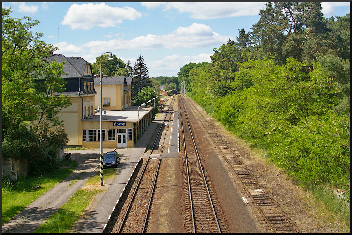 Wenn man den kleinen Bahnhof Doksy so sieht, könnte man meinen irgendwo in einer kleinen Stadt abseits vom regen Leben zu sein. Doch weit gefehlt. So unscheinbar er wirkt, bietet er nur wenige Gehminuten von hier entfernt ein großes Naherhohlungsgebiet mit dem Hirschberger Großteich, der eigendlich ein sehr großer See ist. Nicht weit entfernt liegt die Burg Bezděz, eine gotische Höhenburg.

Doksy liegt im Okres Česká Lípa (Böhmisch Leipa), also in Nordböhmen. Die Stadt lebt hauptsächlich vom Tourismus, meistens den Ausflüglern zum Hirschberger Großteich, da dort auch Campingplätze zur Verfügung stehen.

Mehr über Doksy: https://www.mesto-doksy.cz

Das Foto vom Bahnhof wurde von einer Fußgängerbrücke über die Gleise am 22.05.2022 gemacht.
