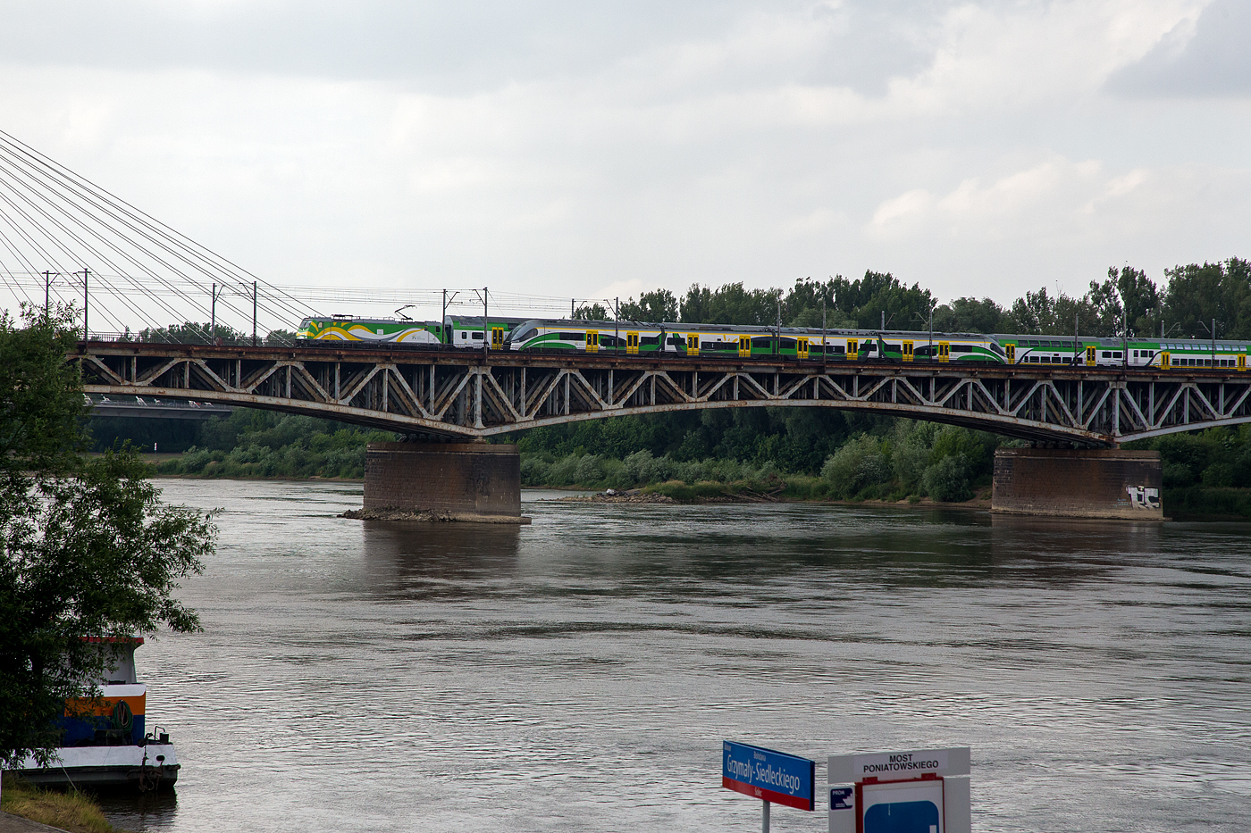 Zwei Züge der KM - Koleje Mazowieckie (Masowische Eisenbahnen) überqueren auf der Most Średnicowy (deutsch: Durchmesserbrücke) in Warschau am 26 Juni 2017 die Weichsel. Vorne ein vierteiliger PESA „Elf“ der Baureihe 22WE / EN76 der Richtung Osten (nach rechts) fährt, dahinter eine EU47 (Traxx P160 DC) mit Bombardier Doppelstockwagen, die Richtung Westen in die Stadt fährt und bald Warszawa Centralna (Warschau Zentralbahnhof) erreicht.