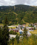 Ganz so schlimm (aus der Ferne), wie Stefan es beschreibt, finde ich es nicht.
Blick auf den neuen ÖV-Hub Fiesch am 07 September 2021 aus einem MGB-Zug. Ein Jahrhundertbau in Fiesch, MGB Bahnhof (1.063 m ü.M.) und Bus-Terminal mit dem direkten Zugang zur Talstation der neuen 10er-Kabinenbahn der Doppelmayr/Garaventa-Gruppe hinauf auf die Fiescheralp. 

Die neue 10er-Gondelbahn Fiesch - Fiescheralp / Kühboden, Baujahr 2019 von der Doppelmayr/Garaventa-Gruppe ist mit 7 m/s Fahrgeschwindigkeit die schnellste 10er-Gondelbahn der Schweiz. Sie ist eine sogenannte D-Line-Bahn der Doppelmayr/Garaventa-Gruppe mit Seillageüberwachung RPD. Als Betriebsmittel kommen die neuen CWA Kabinen Omega V zum Einsatz. Als Antrieb wurde der 867 kW starke Doppelmayr Sector Drive (DSD) verwendet, ein permanenterregter Synchronmotor, der mit modernster Frequenzumrichtertechnologie arbeitet und sich auch für steile Anlagen wie die hier in Fiesch sehr gut eignet.

Die neue Gondelbahn ersetzt zwei Pendelbahnen von Fiesch zur Fiescheralp, einmal mit 100er-Kabinen und einmal mit 34er-Kabinen. Die Talstation der hochmodernen Anlage befindet sich im neuen ÖV-Hub (Knotenpunkt Öffentlicher Verkehr) in Fiesch, wo direkter Anschluss an die Matterhorn-Gotthard-Bahn und das Postautonetz besteht.

Ein Ausbau der Bahn mit einer zweiten Sektion vom Kühboden Richtung Eggishorn als Ersatz für die Luftseilbahn Fiesch-Eggishorn ist angedacht und bereits genehmigt.

Immer mehr Skitouristen nutzen den öffentlichen Verkehr für die Fahrt in den Wintersport. Voll diesem Trend entsprechend haben die Aletsch Bahnen, die Matterhorn-Gotthard-Bahn (MGB) und die Gemeinde Fiesch als Bauherren mit dem Architekten und Investor Hans Ritz die neue ÖV-Drehscheibe in Fiesch als Gemeinschaftsprojekt gebaut. Der neue Verkehrsknotenpunkt besteht aus der Talstation der neuen 10er-Kabinenbahn auf die Fiescheralp, einem komplett neuen Bahnhof der MGB und einem Postbus-Terminal. Durch die Integration und Verknüpfung aller Verkehrsträger an einem Ort wurden kurze, schnelle und barrierefreie Umsteigwege geschaffen.

Für das Projekt hat die MGB den Haltepunkt für ihre Züge vom bisherigen Bahnhofsgebäude 400 m nach Norden verlegt und in den ÖV-Hub integriert. Dadurch ist ein komplett neuer Bahnhof mit zwei Außenbahnsteigen sowie einem 600 m langen neuen Doppelgleis für eine optimierte Kreuzungsmöglichkeit der Züge entstanden. Eine besondere Herausforderung bei der Gleisverlegung stellte die 36 m lange Bogenweiche mit einem Gewicht von 35 t dar. Sie wurde in drei Teilen angeliefert und dann mit einem Kran über die Dächer gehievt und eingebaut.

Die neue Kabinenbahn ersetzte die 100er-Pendelbahn Fiesch – Fiescheralp (Kühboden) von Garaventa aus dem Jahr 1974. Für die neue Bergstation wurde die bestehende Bausubstanz der abgebauten Pendelbahn erweitert und für die Garagierung der Kabinen verwendet. Bei der Talstation wurden 760 m“ und bei der Bergstation 1.100 m² Kunststoff-Folie als Fassaden-verkleidung eingesetzt. Die Verkehrswege in den Stationen sind barrierefrei angelegt. Die Bahn ist mit der neuesten Kabinengeneration der Omega V von CWA ausgestattet, für den Gütertransport stehen zwei Transportkabinen zur Verfügung.

Der ÖV-Hub Fiesch wurde nach einer äußerst kurzen Bauzeit von 14 Monaten am 7. Dezember 2019 feierlich eröffnet. Mit rund 24 Mio. CHF übernahm die Aletsch Bahnen AG den Hauptanteil dieser Investition. Die MGB beteiligte sich mit 17,6 Mio. CHF, der Architekt Hans Ritz investierte 6 Mio. Das Vorzeigeprojekt ÖV-Hub Fiesch macht eindrucksvoll deutlich, was durch Kooperation von verschiedenen Partnern erreicht werden kann.

TECHNISCHE DATEN der Seilbahn:
Hersteller:  Garaventa  (Doppelmayr/Garaventa-Gruppe)
Typ: 10er Gondelbahn (Ein-Seil-Umlaufbahn)
Baujahr: 2019
Höhe der Talstation:1.083 m ü. M.
Höhe der Bergstation: 2.227 m ü. M.
Höhendifferenz: 1.144 m
Abstand zwischen Tal- und Bergstation: 2.698 m
Anzahl der Stützen: 15
Förderseildurchmesser: 56 mm
Antriebsstation: Berg (Spanneinrichtung Tal)
Motorleistung: 867 kW (im Betrieb) / 1.124 kW (beim Anfahren)
Geschwindigkeit:  7 Meter pro Sekunde
Effektive Fahrzeit: 7:48 Minuten
Förderleistung: 1.880 Personen pro Stunde
Kabinenanzahl: 48 und 2 Transport-/Güterkabinen
Kabinentyp: CWA Omega V
